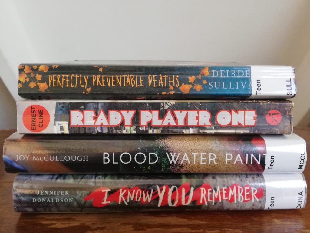 Ashley has plenty of books to read thanks to making a hasty trip to the library before it closed. Titles in the picture include Perfectly Preventable Deaths; Ready Player One; Blood Water Paint; I Know You Remember.